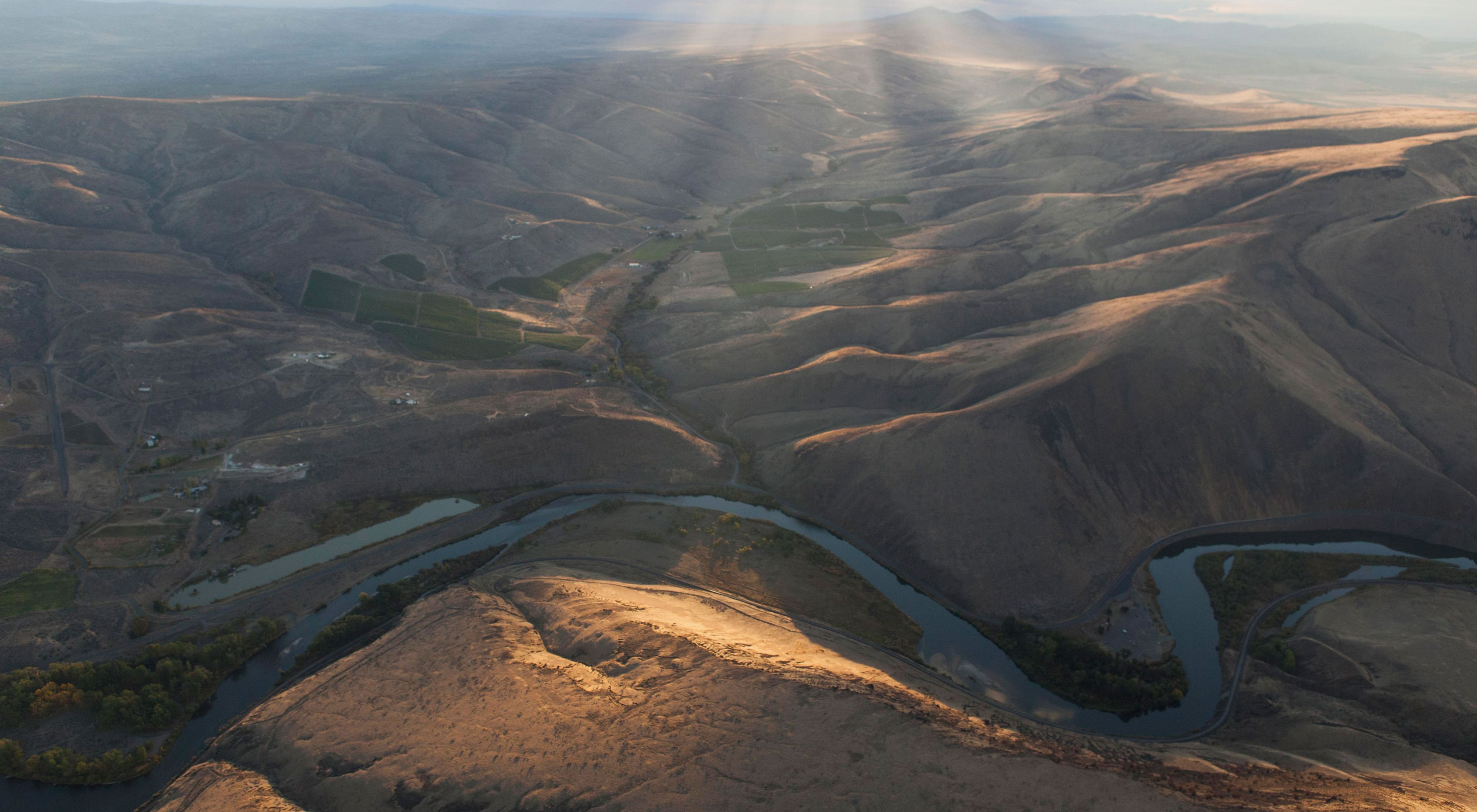 Aerial view of sunlight rays casting a shadow over arid hills and winding river.
