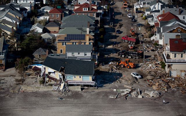 Aerial view of destruction caused by Hurricane Sandy. Rows of houses facing a beach show varying degrees of damage. In the foreground a yellow house is split in two.