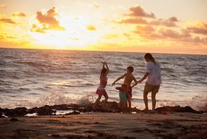 A family with young children enjoys splashing in the water along the ocean shore at sunset.