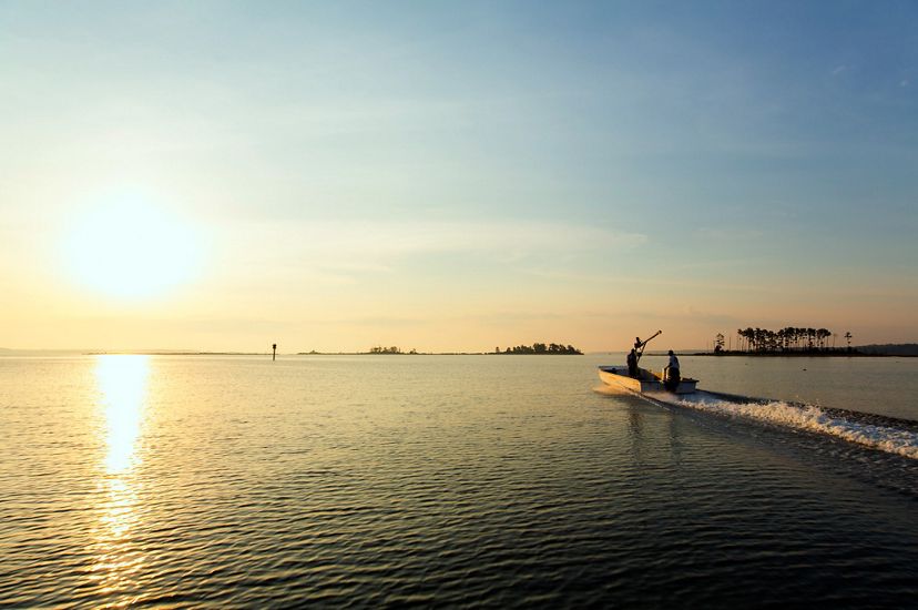 Two men in a low profile john boat motor out into the Chesapeake Bay as the sun rises over the water.