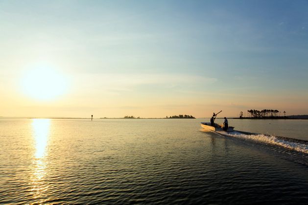 Two men in a small john boat motor out into the Chesapeake Bay as the sun rises over the water.