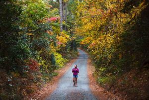 A smiling woman walks along a gravel trail surrounded by fall trees.