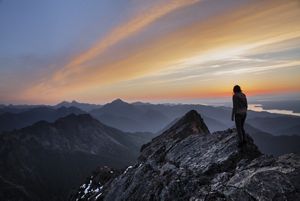 A hiker stands on a rocky outcrop looking out over mist shrouded peaks that stretch to the horizon.