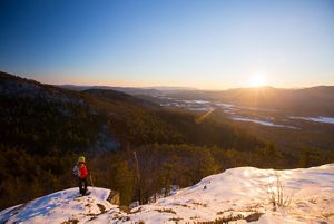 A snowshoer stands at the top of a snowy mountain overlook.