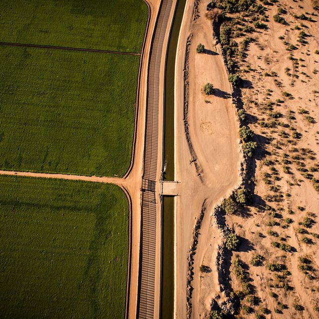 Green U.S. farmland separated from the dry desert by the USA/Mexican border and an irrigation canal.      