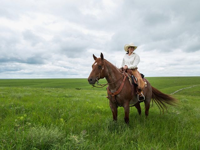 A woman rides a horse through a tallgrass prairie under a sky filled with low clouds.