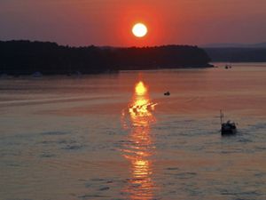 A boat chugs through a bay at sunset.