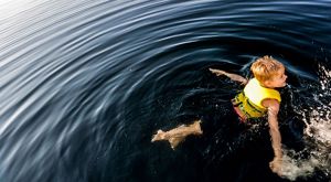 Boy wearing a yellow life jacket swims in a lake.