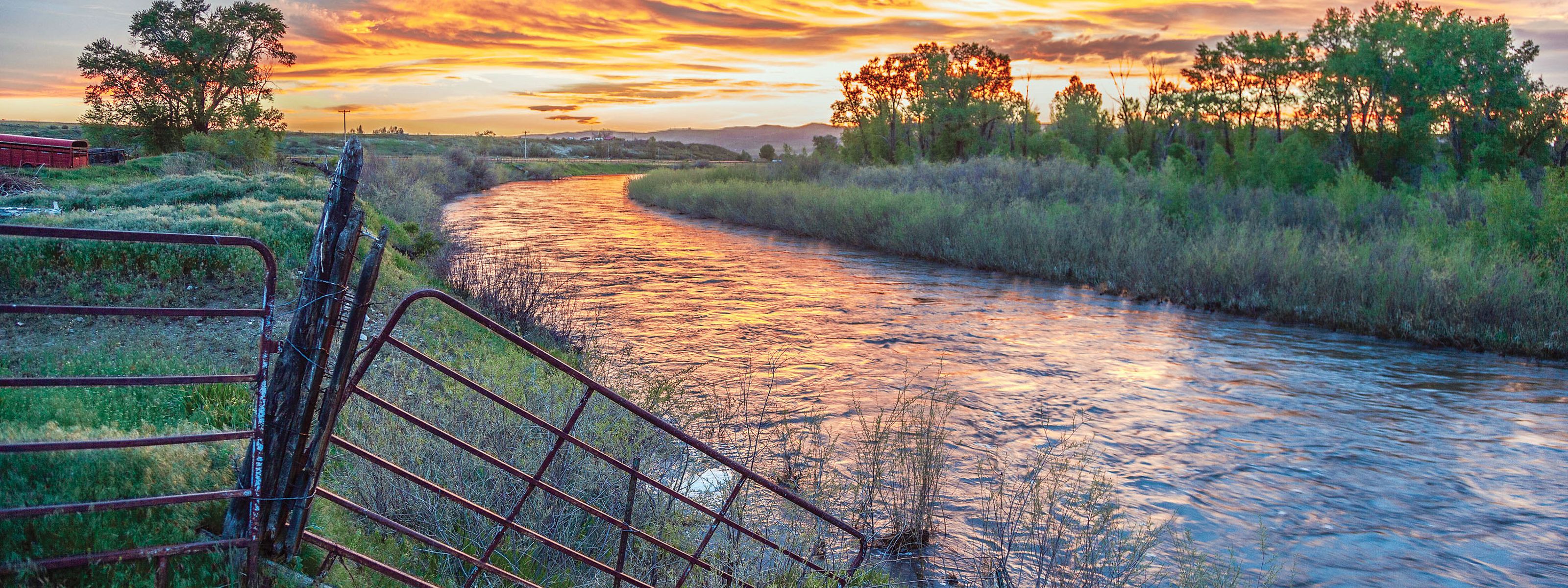 A river flowing through marsh with a bright sunset reflecting on the river.