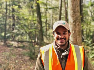 Pabodha Galgamuwa headshot. A smiling man wearing a ballcap and orange and yellow reflective vest stands in a forest.