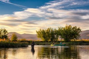 Angler and couple in a canoe floating down a river at sunset.