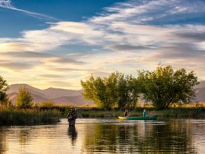 Angler and couple in a canoe floating down a river at sunset.