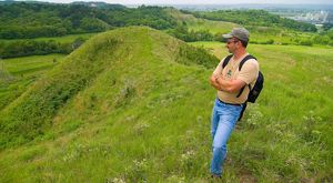 A person stands atop a grassy hill and looks out over the landscape.