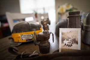 An old photo of two people sitting on the ground with a coal miners helmet and light sitting on the table. 