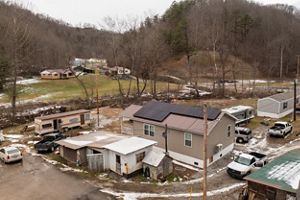 House with solar panels on the roof surrounded by trucks and other buildings. 