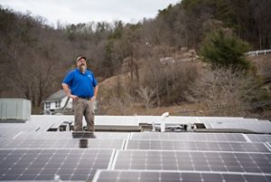 Man standing on a roof surrounded by a solar power installation. 