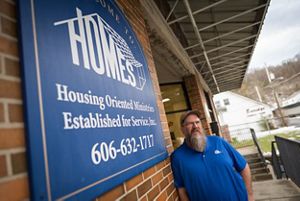Man in a blue shirt posing next to a sign that reads HOMES, Inc. 