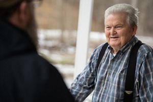 Man standing and smiling wearing a blue plaid shirt. 