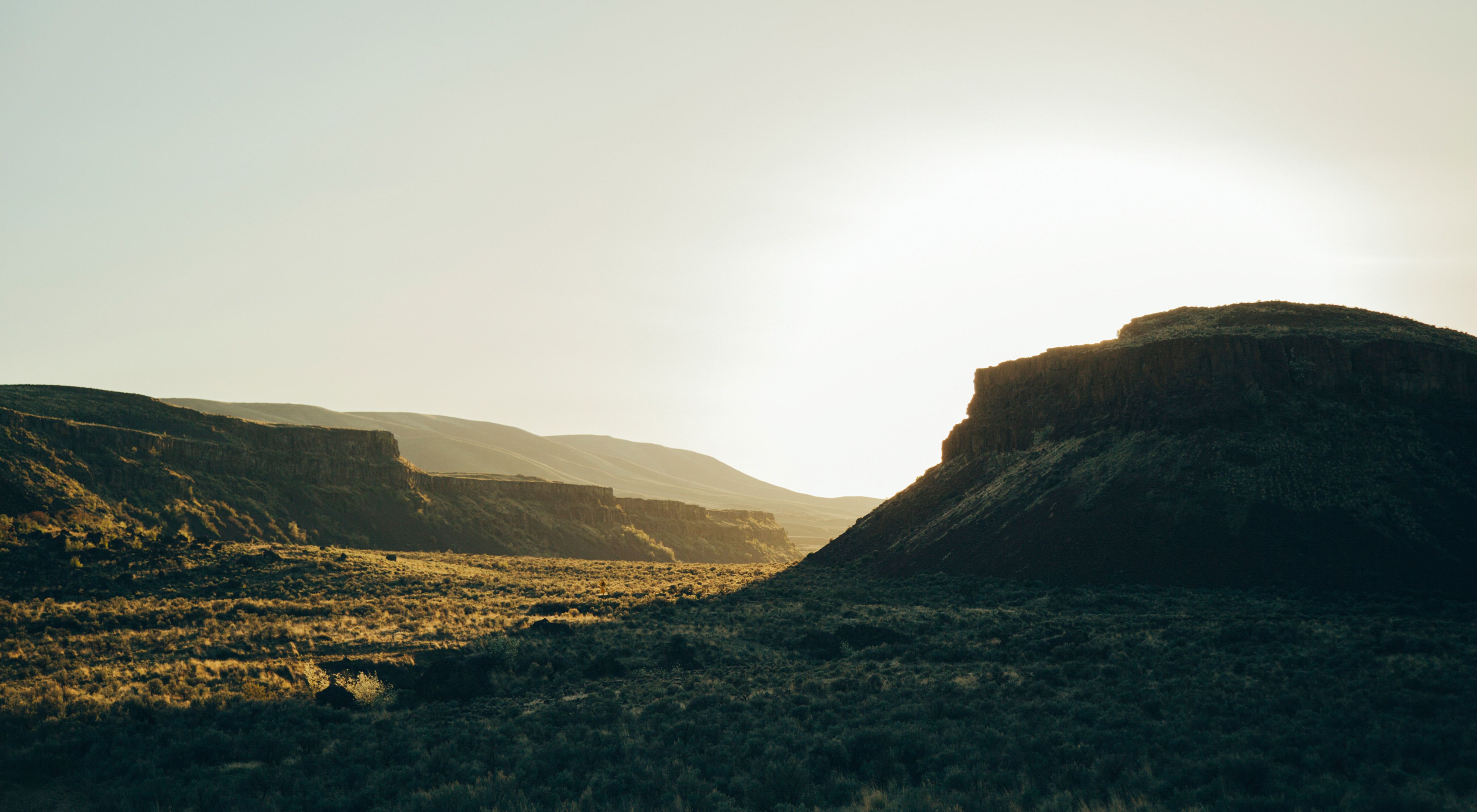 Silhouette of arid, rugged cliffs backlit by sunlight with steppe in the foreground.