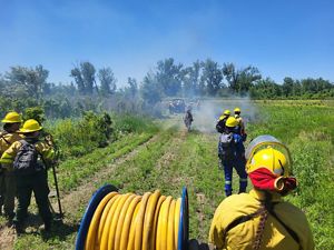 Women stand with fire tools while an ATV drives away.