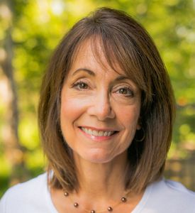 A woman with straight brown hair smiling at the camera. The view is of her head and shoulders.