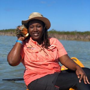 a black woman with a hat holding a queen conch outside
