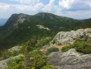 A rocky peak with shrubby green vegetation and a pond close to the summit.