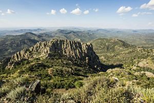 A rocky mountain surronded by jagged crests and rolling hills covered in desert brush.