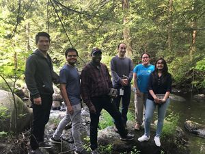 A group of students stands in a forest holding wildlife cameras