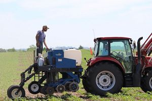 A man stands on top of an agricultural seeder that is attached to a tractor.