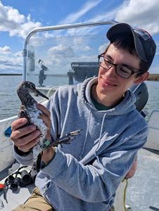Candid portrait of Mario Balitbit sitting in a boat holding a young shorebird.