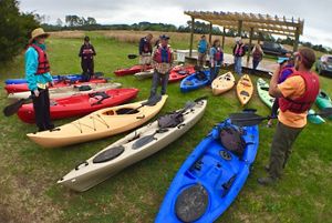 A group of people stand around a collection of kayaks.