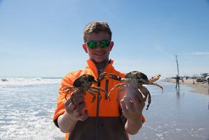 A smiling boy holds up two crabs.