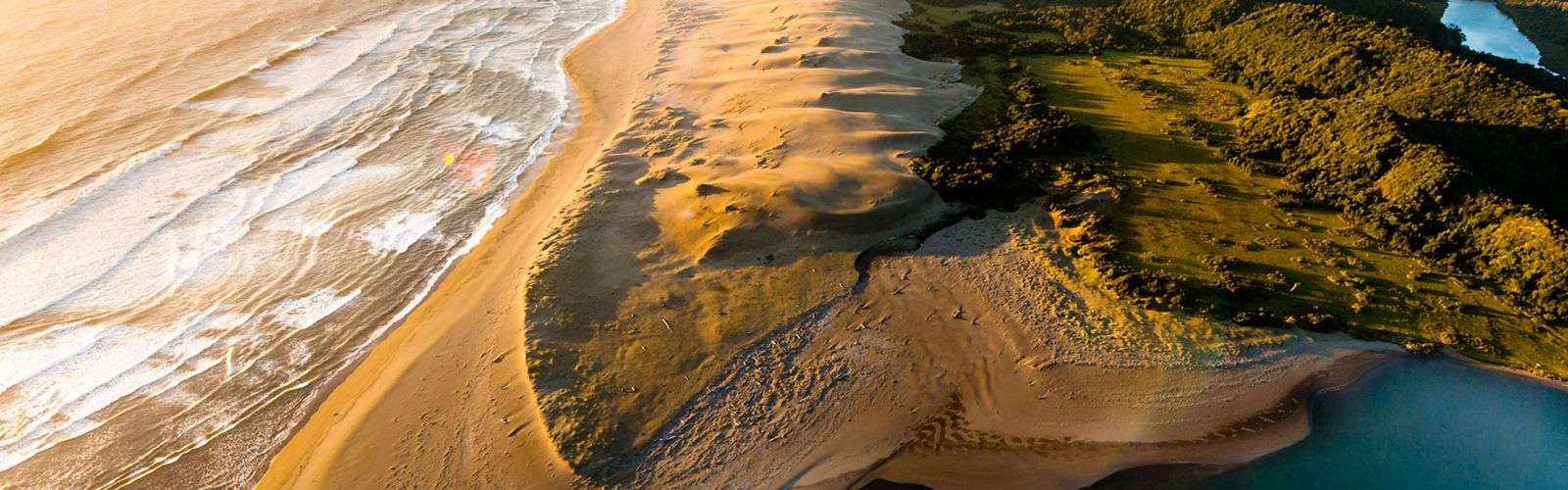 Aerial view of golden sand dunes surrounded by ocean.