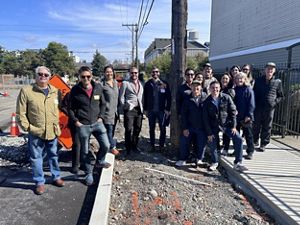A large group of people stand outside on an urban sidewalk and smile for the camera.