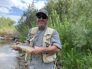 Paul Jewell stands in front of a freshwater stream holding a fish.