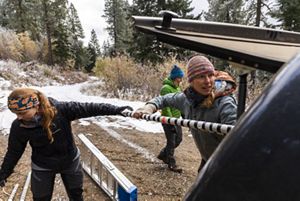 Two people pull equipment out of the back of a vehicle in the middle of a forest.