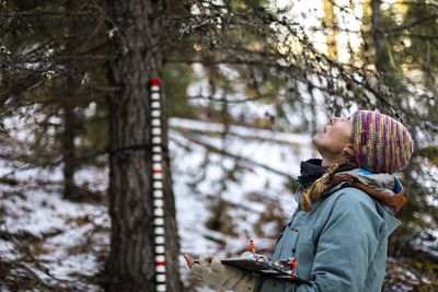 Dr. Emily Howe stands in a forest and looks up at the tops of trees.
