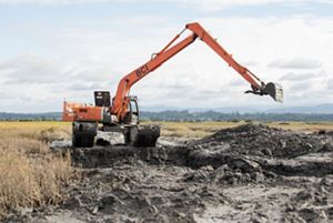 A large orange excavator works to dig a channel in thick mud.
