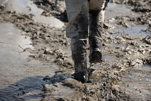 View of the bottom half of a person's legs with tall boots walking through thick mud.