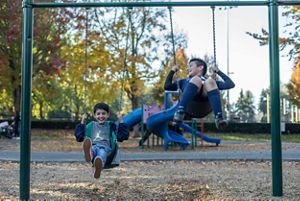 Two children swing on a swingset outdoors.