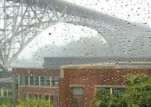 View through a rain-spattered window looking out across brick buildings at a bridge spanning a river.