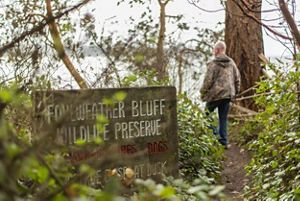 A man walks along a trail and past a sign that reads Foulweather Bluff Wildlife Preserve.