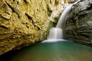 Water rushes over a waterfall into a deep green pool surrounded by rock walls.