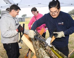 Three people tie big sticks together in a bundle.