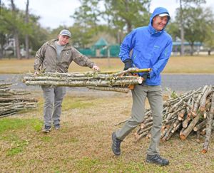 Two people hold either end of a bundle of large sticks.