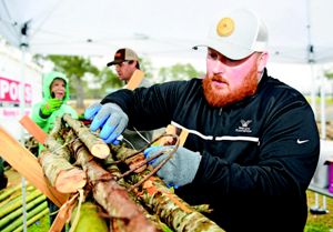 A man wearing a hat and blue gloves ties large sticks into a bundle.