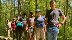 Seven volunteers in brightly colored t-shirts stand in a line on wooden boardwalk, smiling and holding tools.