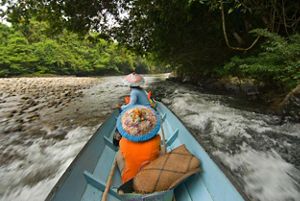 Two women sit in a boat on a speeding river in the jungle.
