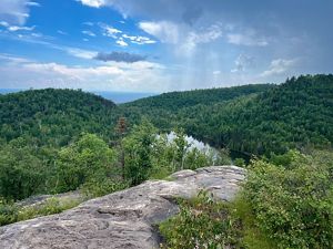 A rocky outcropping overlooking hilly forests and a lake.
